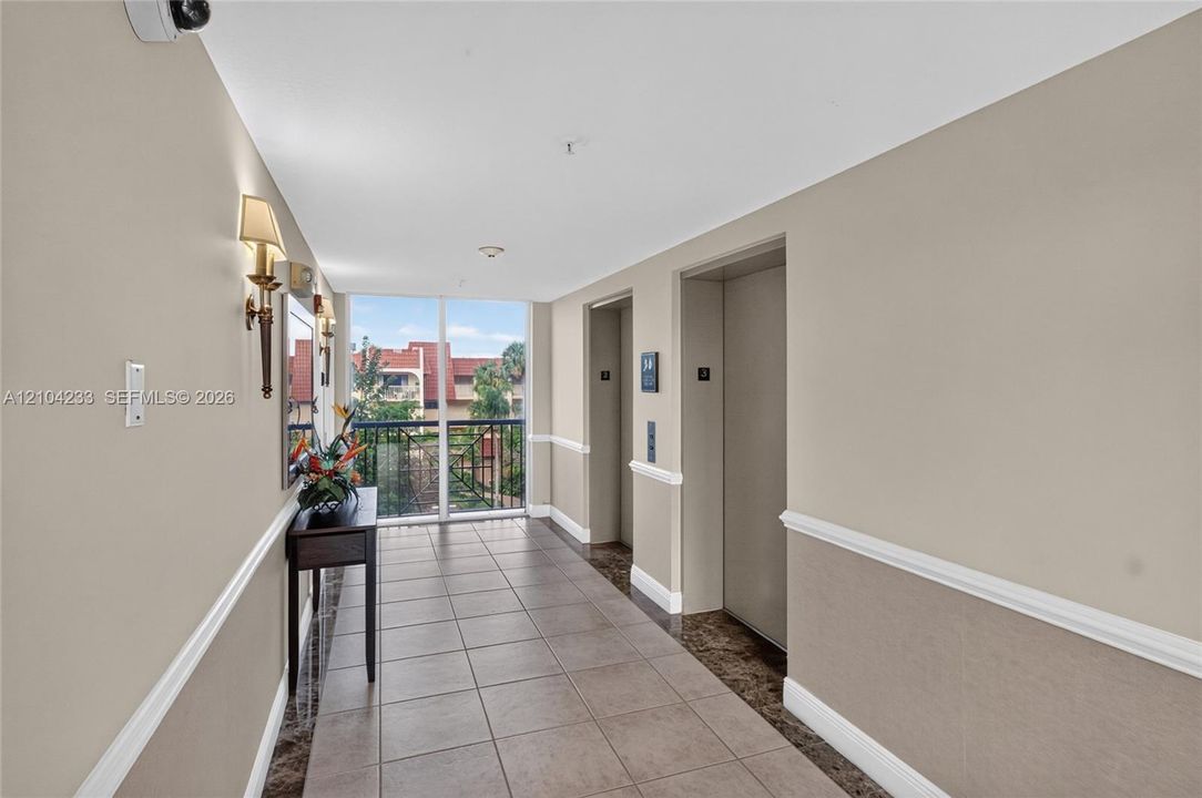 Interior hallway featuring tile flooring, wainscoting, wall-mounted light fixtures, and dual elevator access