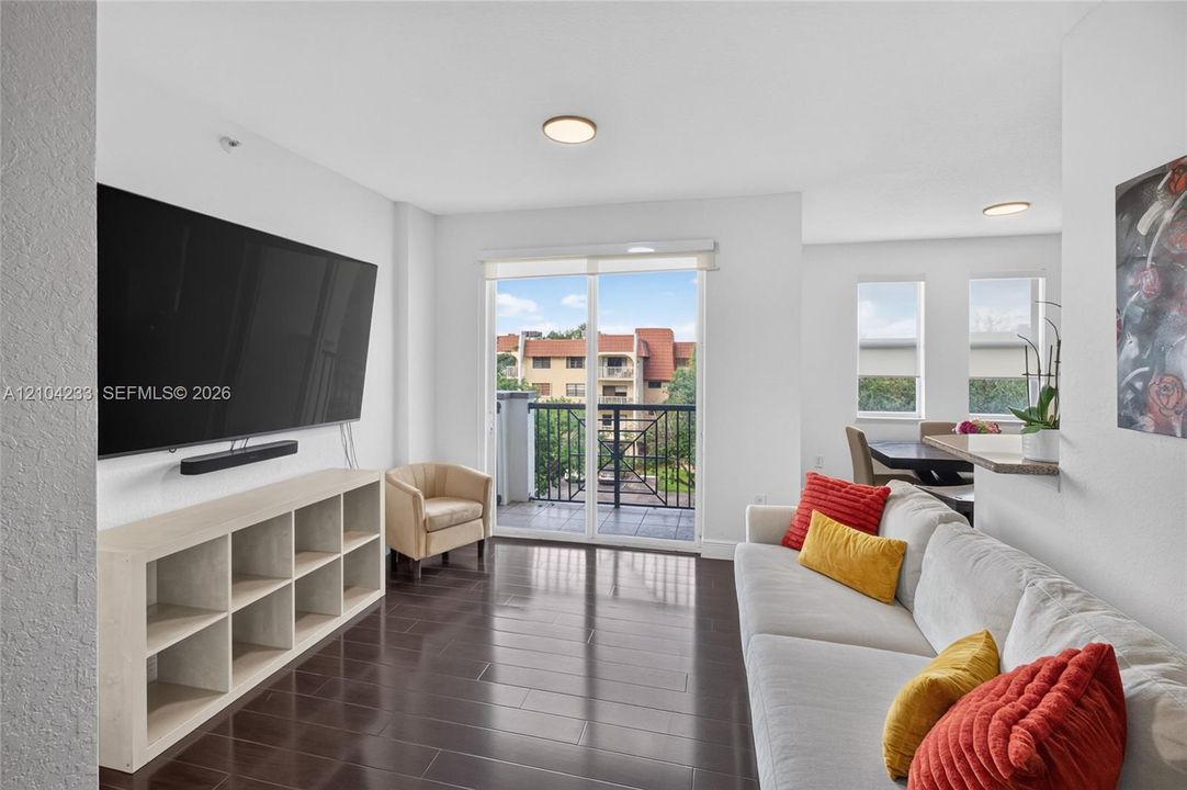 Open living area featuring wood-finish flooring, recessed lighting, and a glass-paneled sliding door providing access to a balcony with metal railings