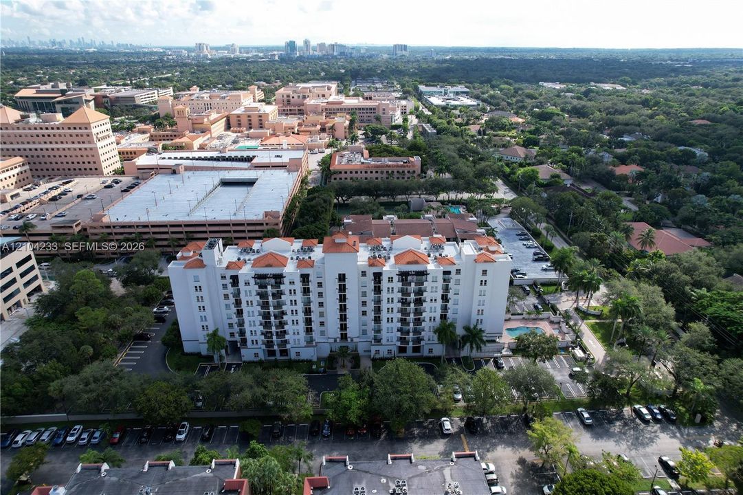 Mid-rise residential building featuring a terracotta tile roof, white stucco facade, multiple private balconies, on-site surface parking, and a ground-level swimming pool