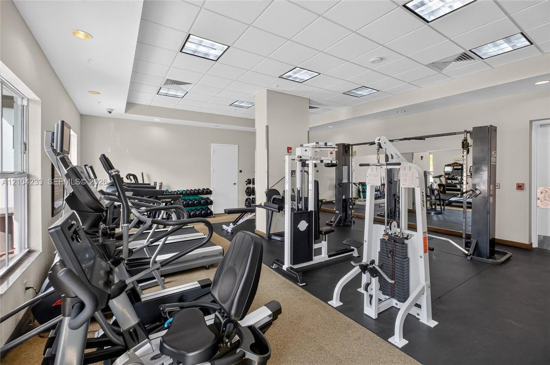Fitness center featuring drop ceiling tiles, recessed lighting, wall-to-wall rubber flooring, and large mirrored walls