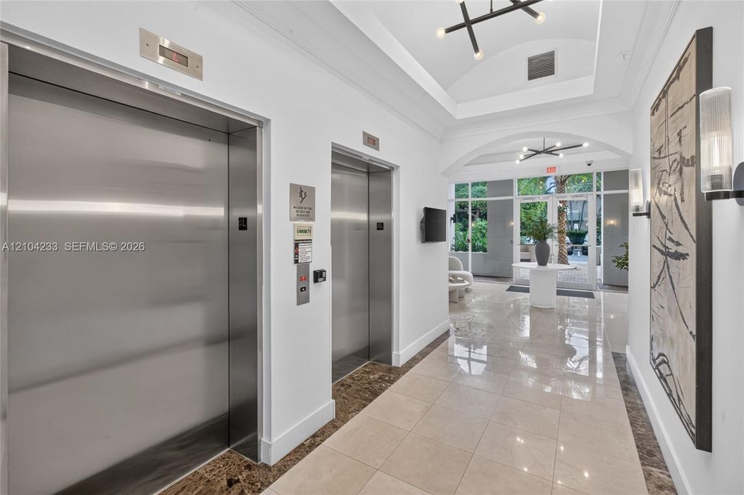 Lobby featuring stainless steel elevators, polished tile flooring, arched ceiling details, and contemporary multi-arm light fixtures