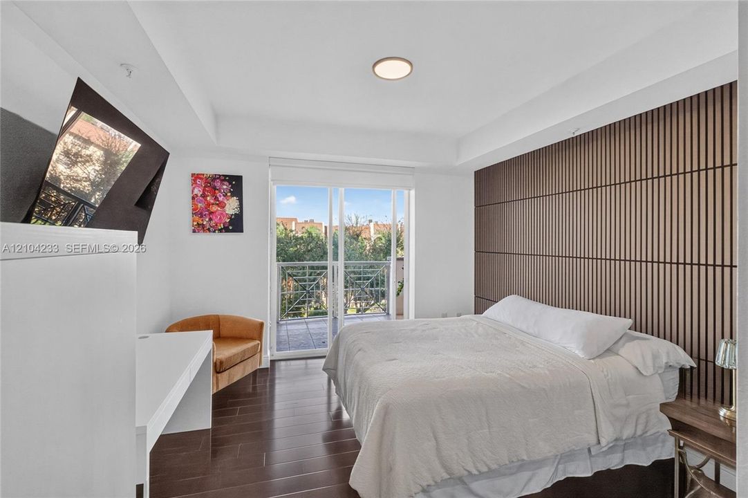 Slatted wood-finish feature wall, wood-finish flooring, tray ceiling with recessed lighting, and a glass-paneled sliding door opening to a private balcony