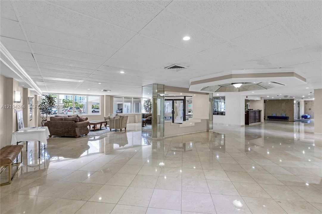 Expansive common area featuring polished stone flooring, recessed lighting, mirrored structural columns, and large windows