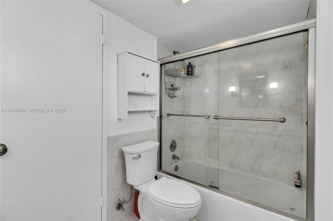 Bathroom featuring a white toilet, wall-mounted storage cabinet, and a bathtub with a glass sliding enclosure