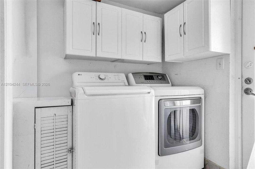 Laundry area featuring white shaker-style wall-mounted cabinetry, built-in lower storage with louvered door, and stainless steel hardware