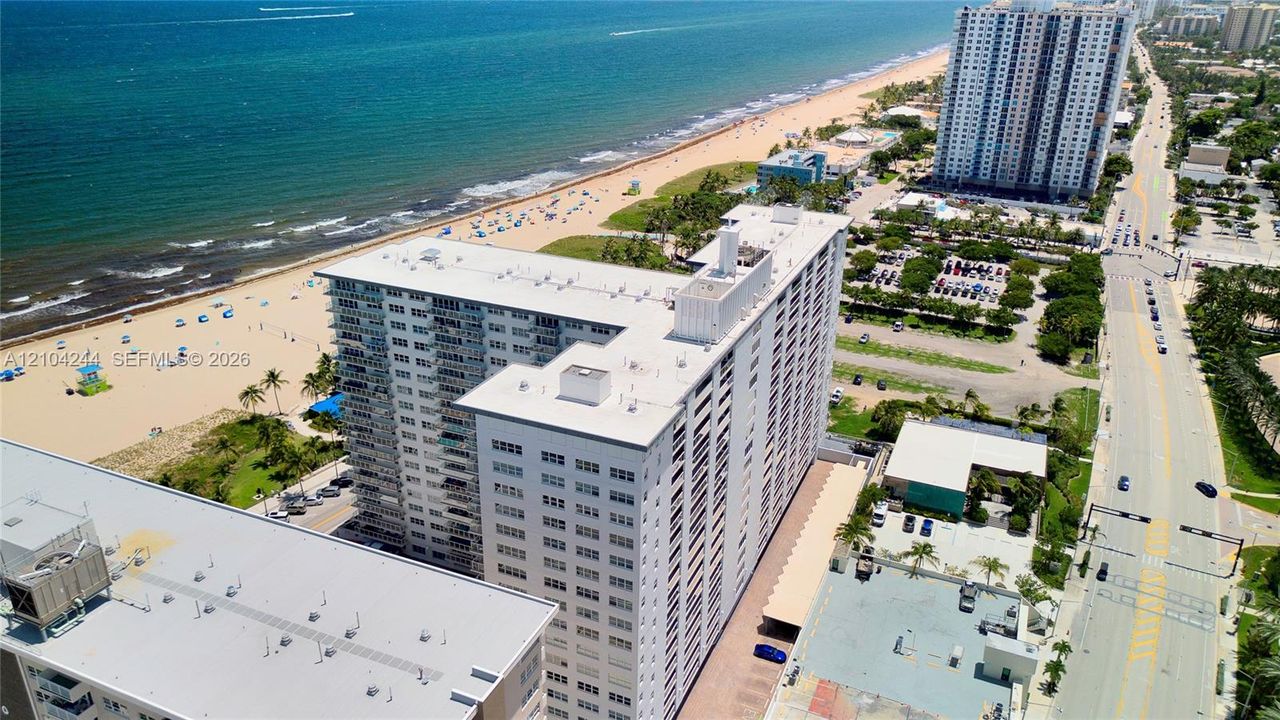 High-rise structure featuring exterior balconies, a flat roofline, and covered surface parking, situated along a coastal coastline