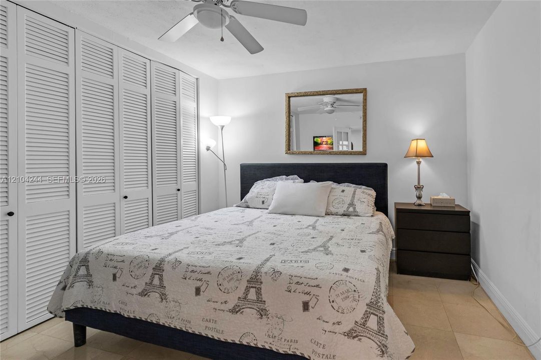 Floor-to-ceiling white louvered closet doors, neutral stone-finish flooring, and a ceiling-mounted fan with light fixture