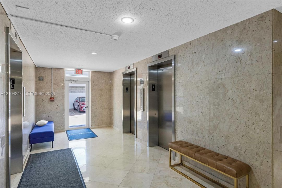 Lobby area featuring full-height natural stone wall cladding, polished stone flooring, and dual stainless steel elevator doors
