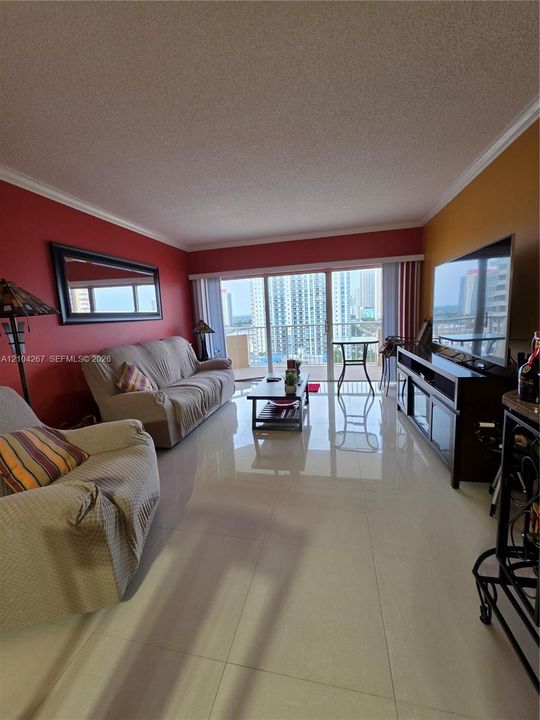 Living area featuring large-format tile flooring, crown molding, and floor-to-ceiling sliding glass doors opening to an outdoor balcony