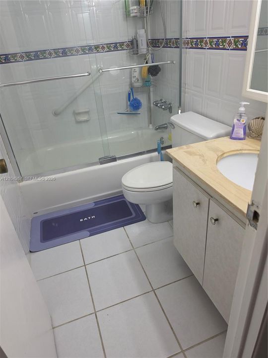 Bathroom featuring a vanity with a countertop, tiled walls with a decorative accent border, a shower-tub combination with sliding glass doors, and tiled flooring