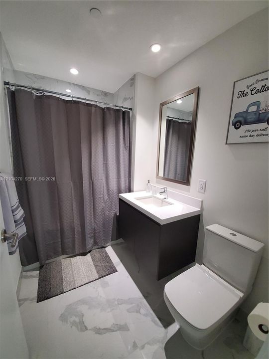 Bathroom featuring a vanity with an integrated rectangular sink and solid surface countertop, large-format tile flooring with a marble-style finish, recessed ceiling lighting, and a framed mirror