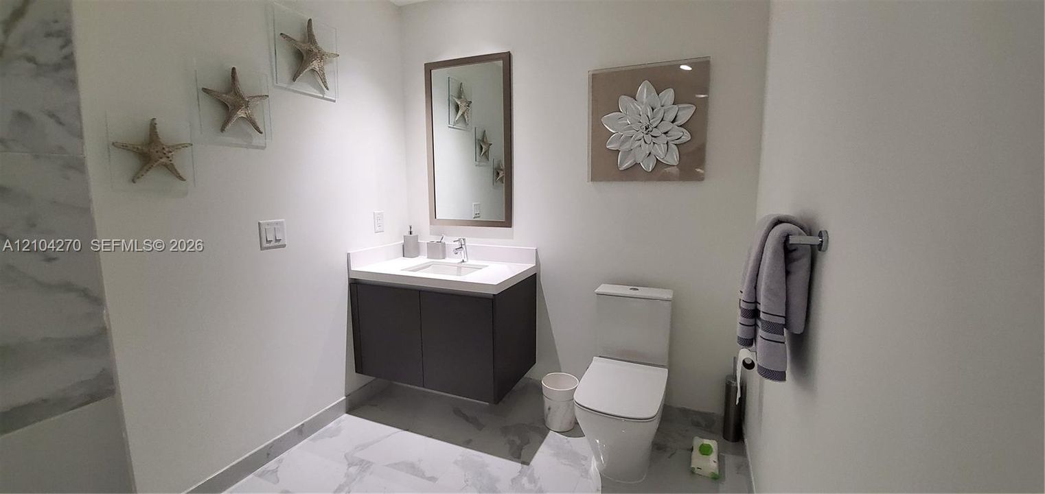 Floating vanity with a white countertop and integrated sink, framed rectangular wall mirror, two-piece toilet, and tile flooring