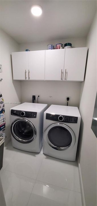 Laundry area featuring white wall-mounted cabinetry with metal hardware, tiled flooring, and recessed ceiling lighting