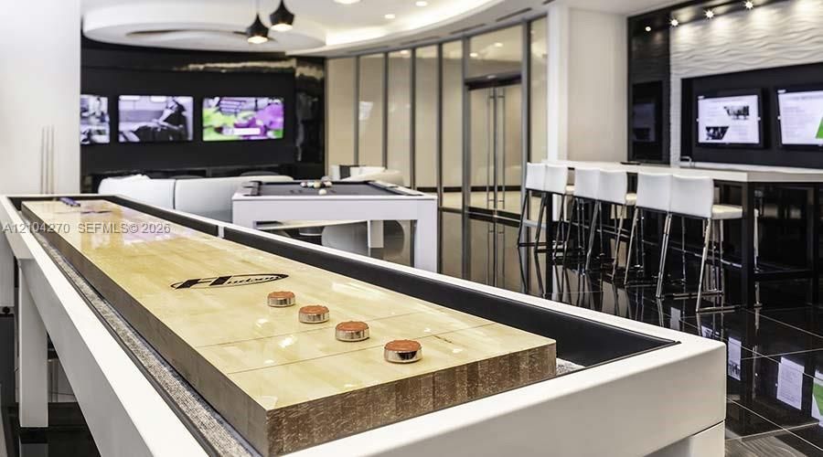 Recreation space featuring polished tile flooring, recessed circular ceiling architecture, built-in display screens, glass-enclosed partitions, and multi-level bar seating