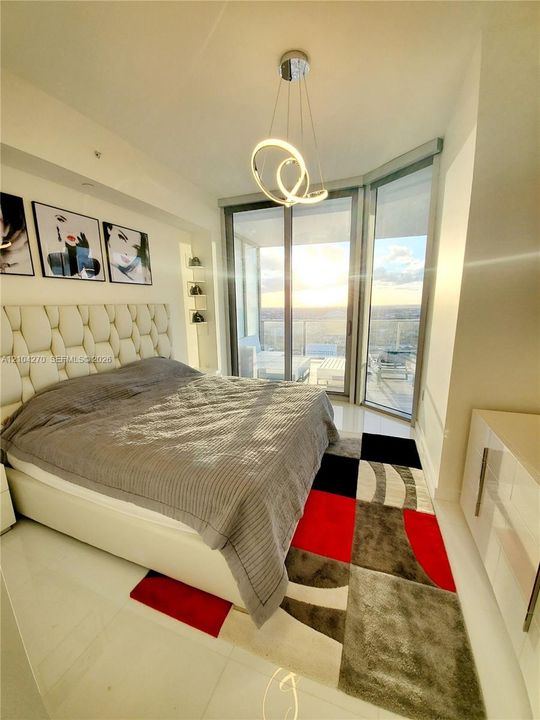 Floor-to-ceiling glass sliding doors opening to an exterior balcony, modern circular LED pendant light, built-in shelving niches, and polished tile flooring