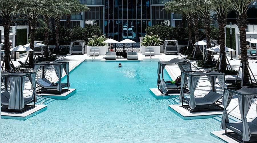 Swimming pool featuring integrated cabanas, expansive sun deck, mature palm trees, and raised water-level platforms