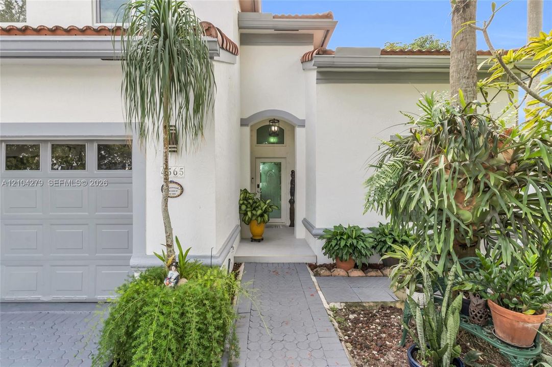 Stucco exterior featuring arched entryway, terracotta roof accents, decorative trim, and paved stone walkway