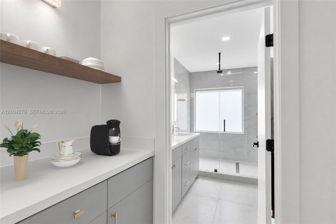 Built-in grey cabinetry with solid surface countertops, floating wood shelf, and recessed lighting, featuring an entry to a walk-in shower with glass enclosure and large-format tile flooring
