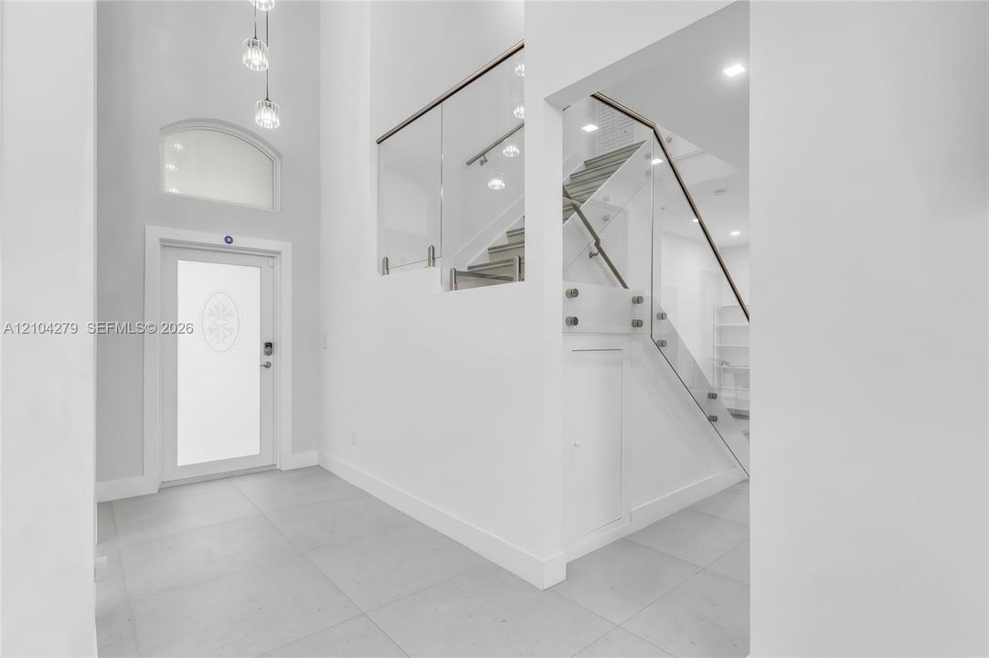 Foyer featuring double-height ceilings, large-format tile flooring, a glass-panel staircase railing, recessed lighting, and a front entry door with a frosted glass insert