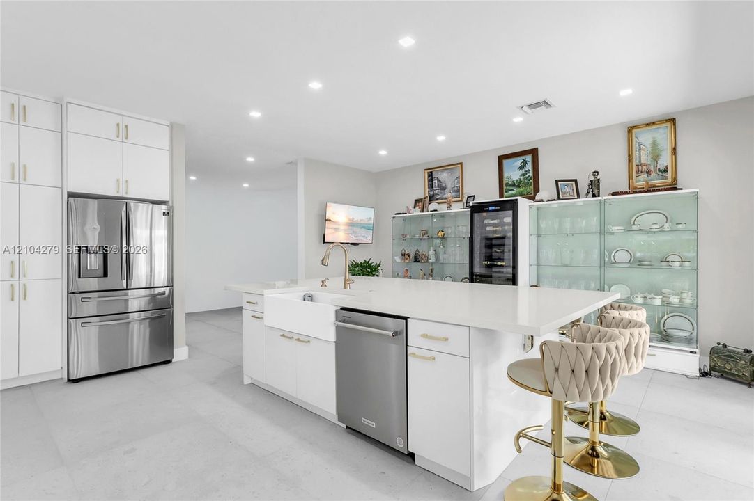 Kitchen featuring white floor-to-ceiling cabinetry, a central island with a solid surface countertop, an apron-front sink, integrated stainless steel appliances, and large-format tile flooring