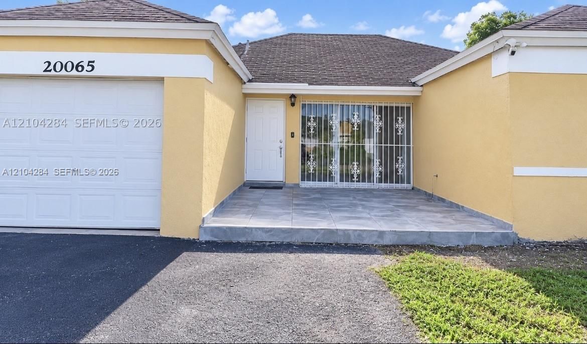 Single-story exterior featuring a stucco facade, an attached garage, and a tiled front patio with metal security screening