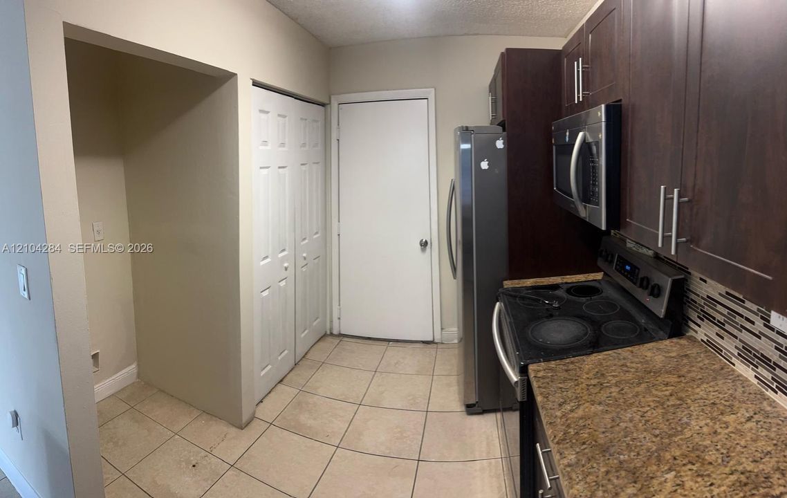 Kitchen featuring dark wood-finish cabinetry, stainless steel appliances, a stone-pattern countertop, tile backsplash, and ceramic floor tiling