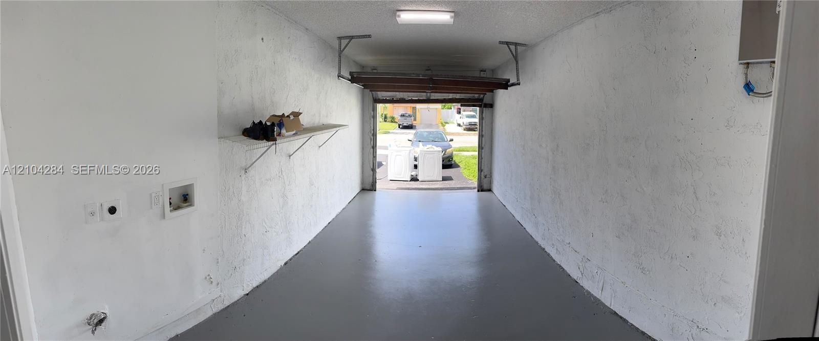 Single-car garage featuring painted textured walls, epoxy-coated flooring, ceiling-mounted lighting, and integrated laundry utility hookups