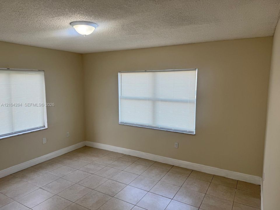 Neutral-toned interior space featuring ceramic tile flooring, two windows with horizontal blinds, and a semi-flush mount ceiling fixture