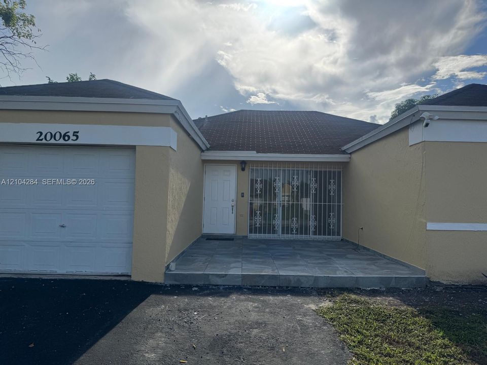 Stucco exterior featuring a single-car garage, stone-tiled front patio, and metal security screening