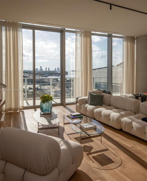 Floor-to-ceiling glass windows, wide-plank wood-finish flooring, metal-framed balcony access, and track lighting