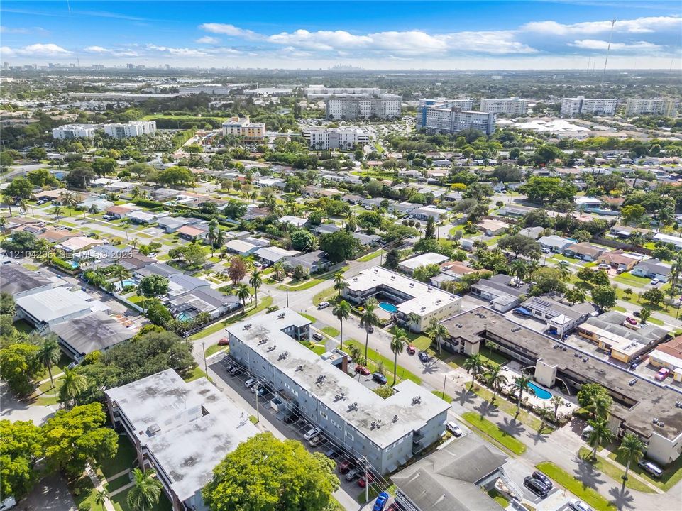 Aerial perspective of a multi-unit residential complex featuring flat roofs, central courtyards with swimming pools, and mature palm landscaping within a dense suburban grid