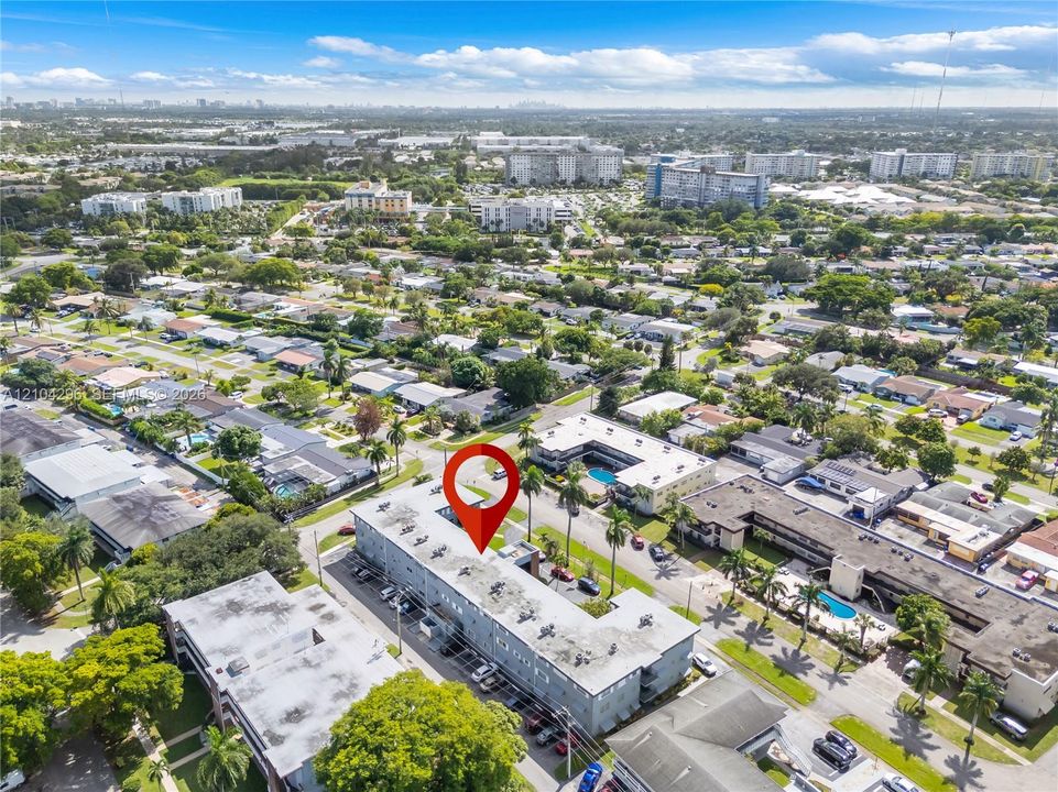 Aerial perspective of a multi-story building featuring an expansive roof surface, designated surface parking, and mature palm tree landscaping