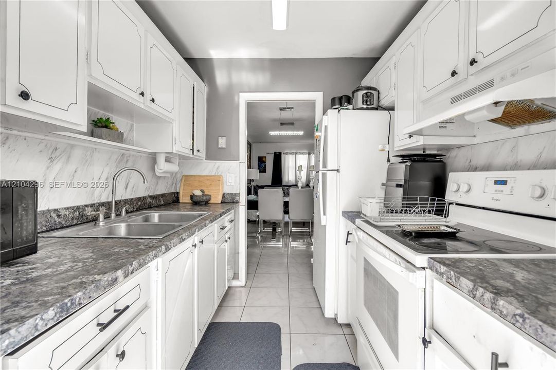 Kitchen featuring white cabinetry, stone-patterned laminate countertops, marble-patterned backsplash, stainless steel dual-basin sink, and ceramic tile flooring