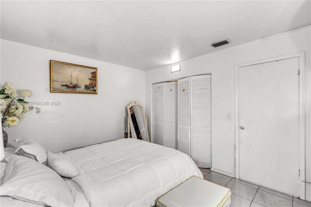Neutral-toned interior space featuring light-colored tile flooring, white walls, and triple-panel louvered closet doors