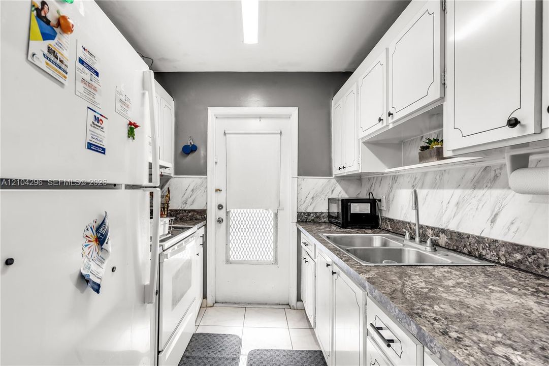 Kitchen featuring white cabinetry, stone-finish laminate countertops, dual-basin stainless steel sink with high-arch faucet, tile flooring, and stone-patterned backsplash