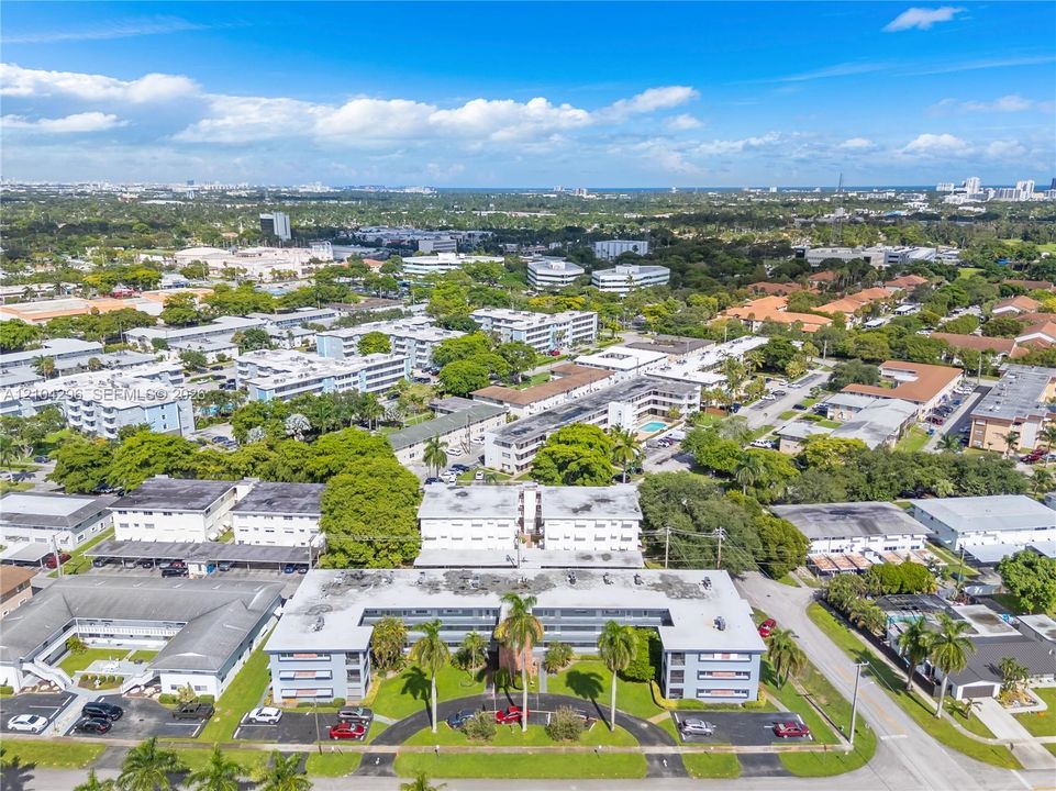 Aerial perspective of a multi-story residential building featuring a circular drive, integrated parking areas, mature palm trees, and landscaped green space
