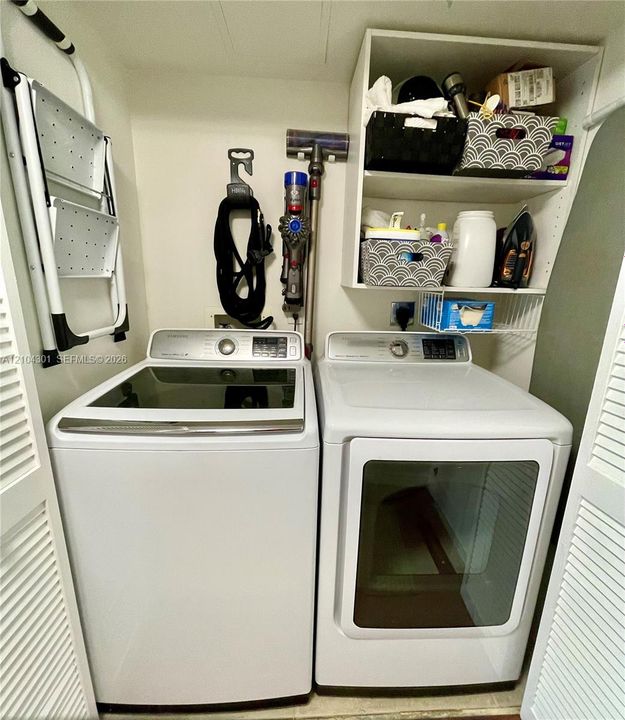 Laundry area featuring top-loading washer and front-loading dryer, built-in upper shelving, and louvered folding doors