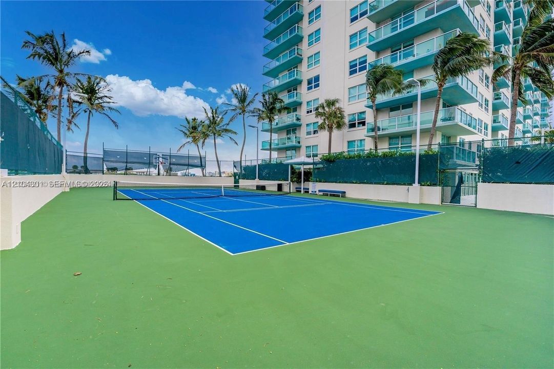 Tennis court with blue surface, perimeter fencing, and surrounding palm trees