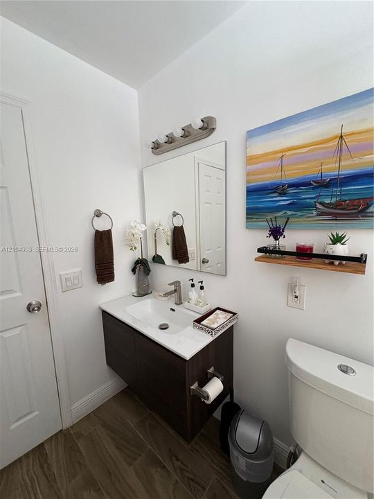 Floating vanity with a white countertop and rectangular basin, integrated mirror, multi-light brushed-nickel fixture, and wood-finish tile flooring