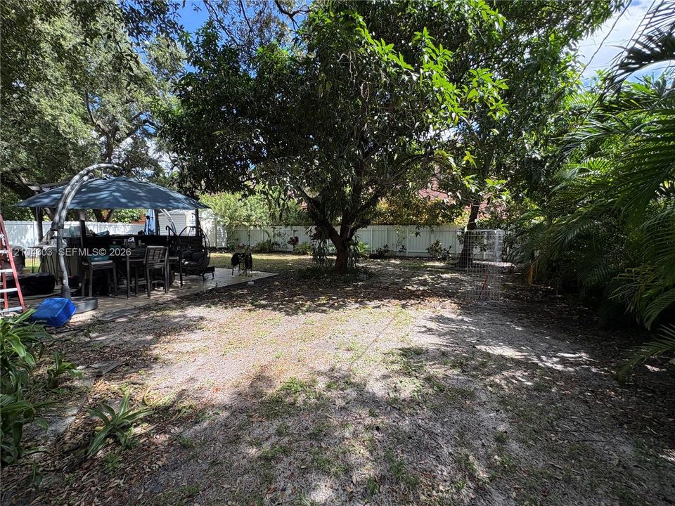 Backyard space featuring a concrete patio, perimeter vinyl fencing, and mature trees
