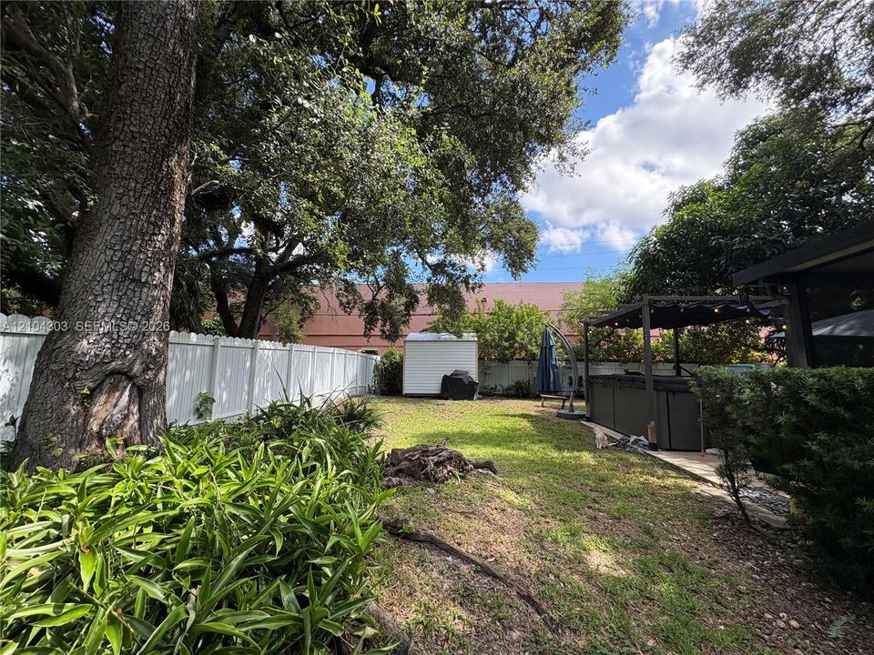 Private backyard featuring a white vinyl privacy fence, mature trees, manicured landscaping, and a covered pergola structure