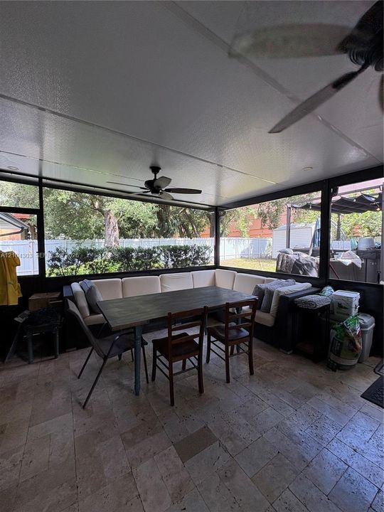 Screened-in patio featuring stone tile flooring, a solid ceiling, and a ceiling fan