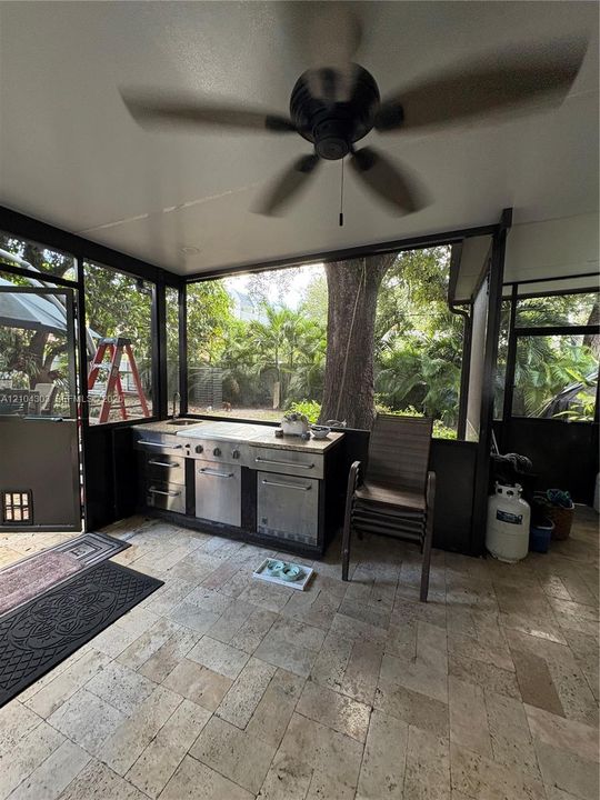 Screened patio featuring stone-tile flooring, a built-in outdoor kitchen with stainless steel appliances, and a ceiling-mounted fan