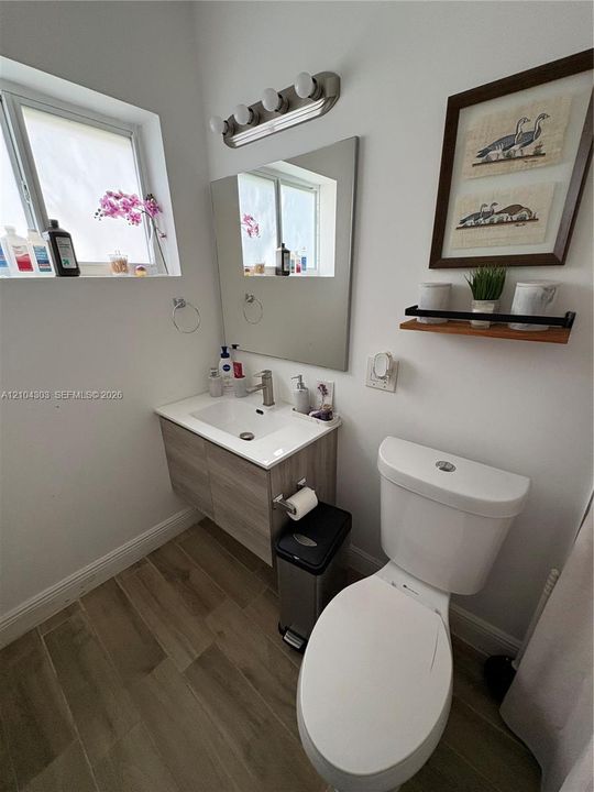 Floating vanity with integrated sink, wood-finish cabinetry, rectangular wall mirror, wood-finish tile flooring, and four-light vanity fixture
