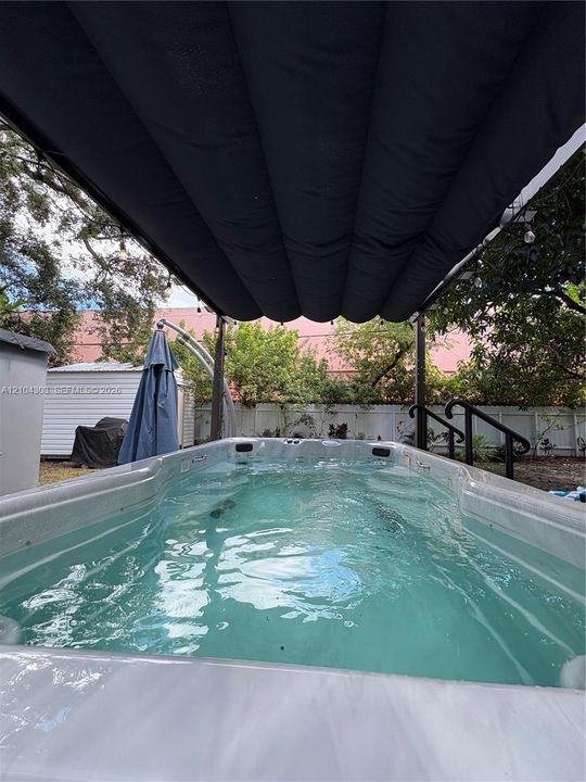 Built-in resistance pool featuring a retractable overhead canopy, integrated steps with black handrails, and surrounding privacy fencing