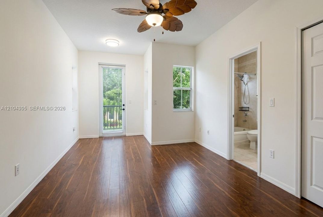 Room featuring wood-finish flooring, ceiling fan with palm-style blades, single-pane windows, glass-panel entry door, and multi-panel interior door