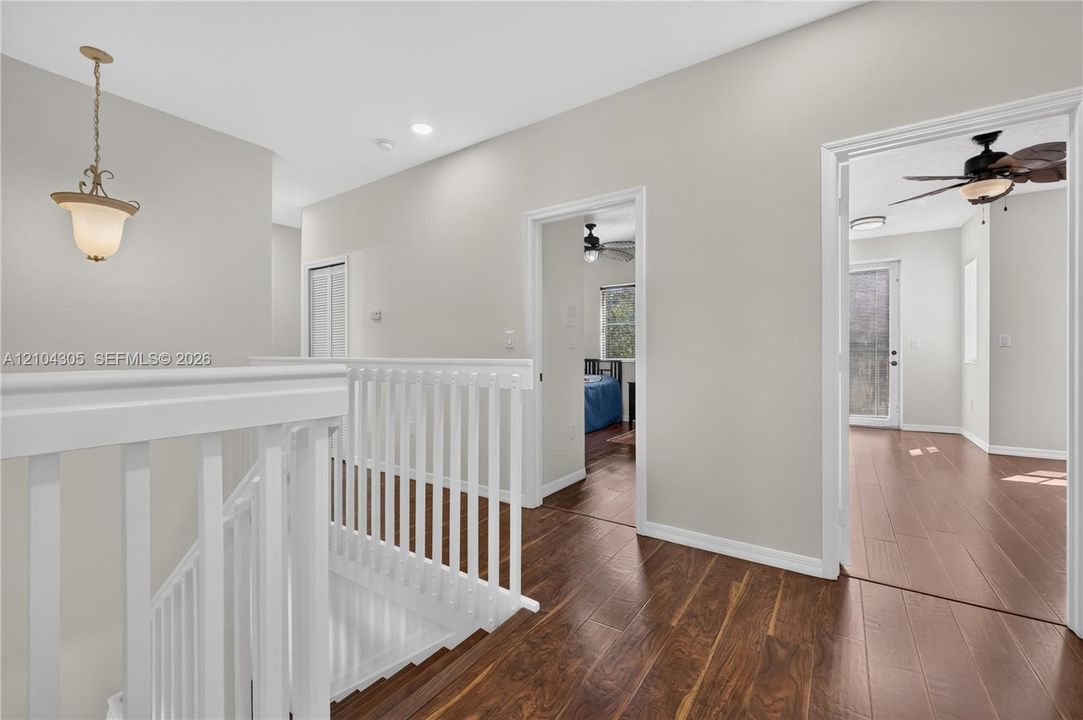 Hallway featuring wood-finish flooring, white spindle balustrades, neutral paint palette, recessed lighting, and a pendant light fixture