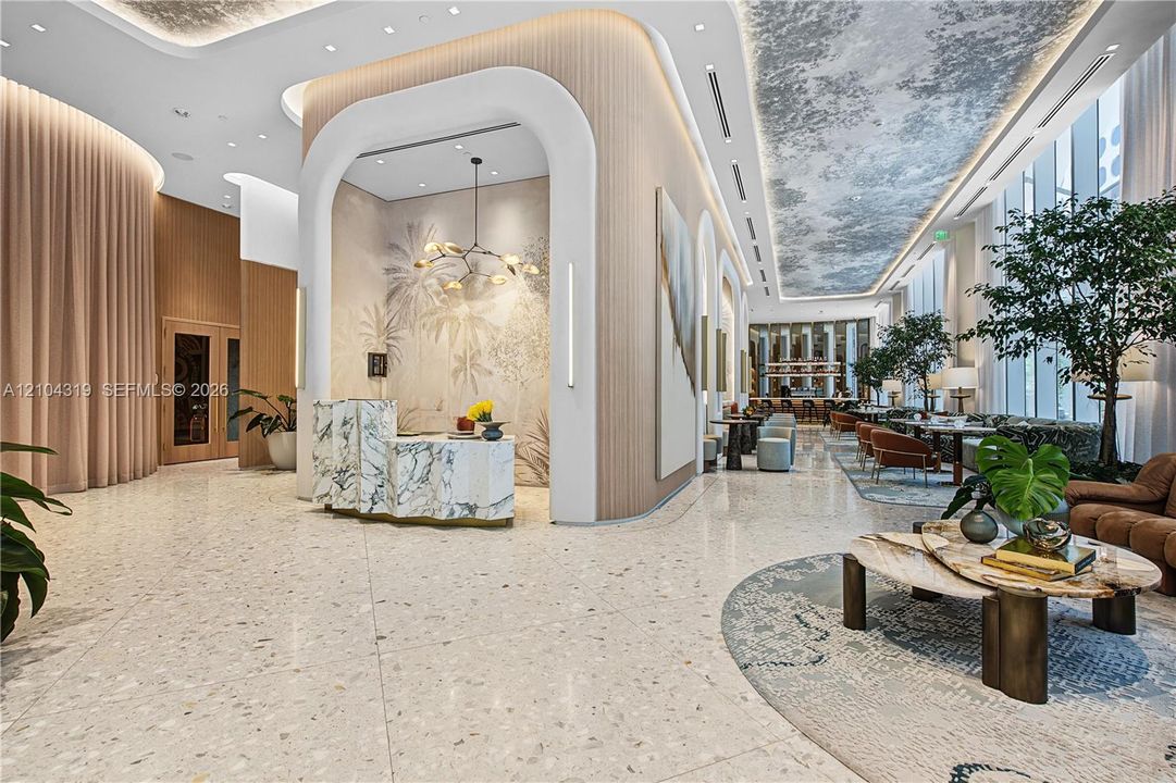 Open lobby featuring terrazzo flooring, fluted wood paneling, arched architectural detailing, a stone-cladding reception desk, and a decorative coffered ceiling