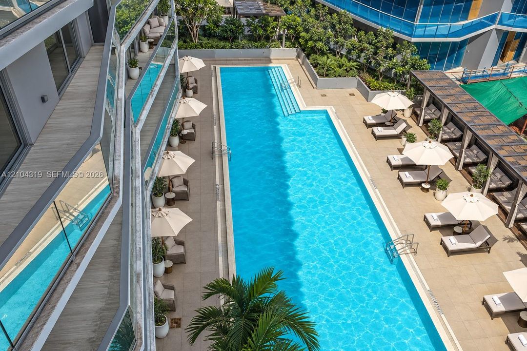 Rectangular swimming pool featuring integrated steps and stone-paved decking, complemented by a shaded pergola structure and landscaped perimeter greenery