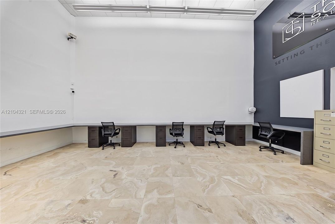 High-ceiling room featuring large-format stone-finish flooring, extensive built-in desk cabinetry, and linear overhead lighting